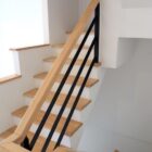 Escalera interior de madera con pasamanos sobre barandilla metálica negra